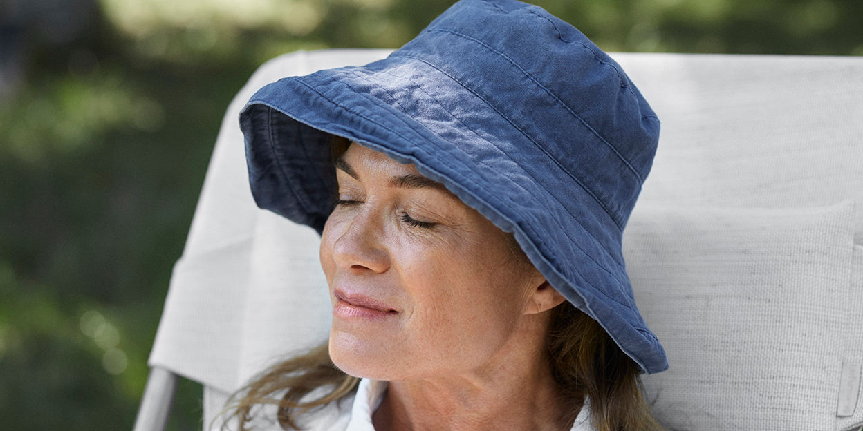 Kvinna sitter i solstorl med solhatt på sig utomhus. 