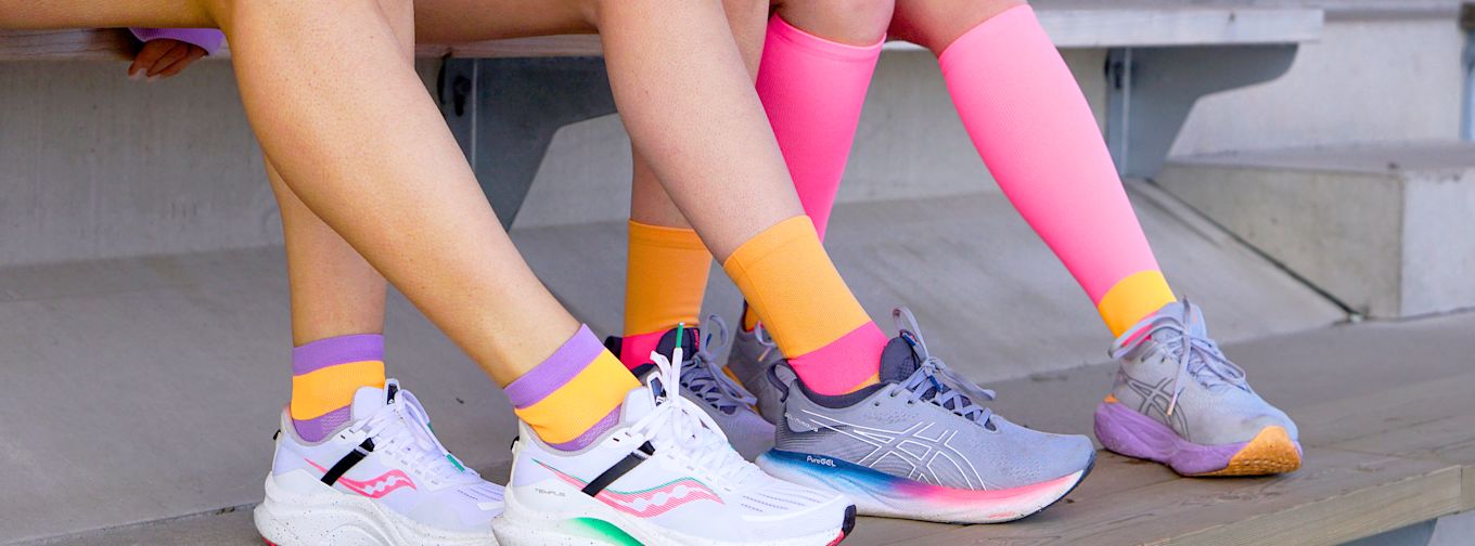 Två personer sitter på en bänk, bär färgglada sportstrumpor och sneakers, benen korsade på en utomhustribun.