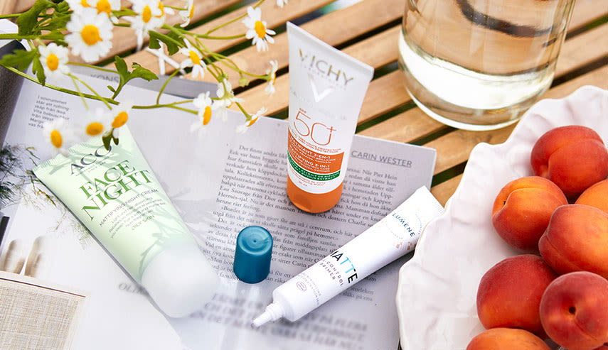 På ett bord ligger produkter från Vichy, ACO och Lumene. Bredvid ligger ett fat med nektariner, en karaff med vatten och en bukett med blommor.