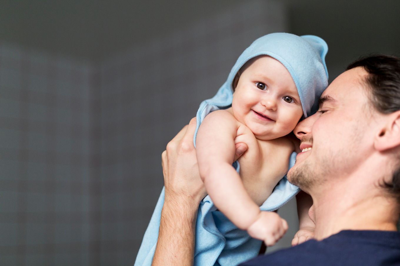 Pappa ler och håller upp nybadad bebis, insvept i handduk. 