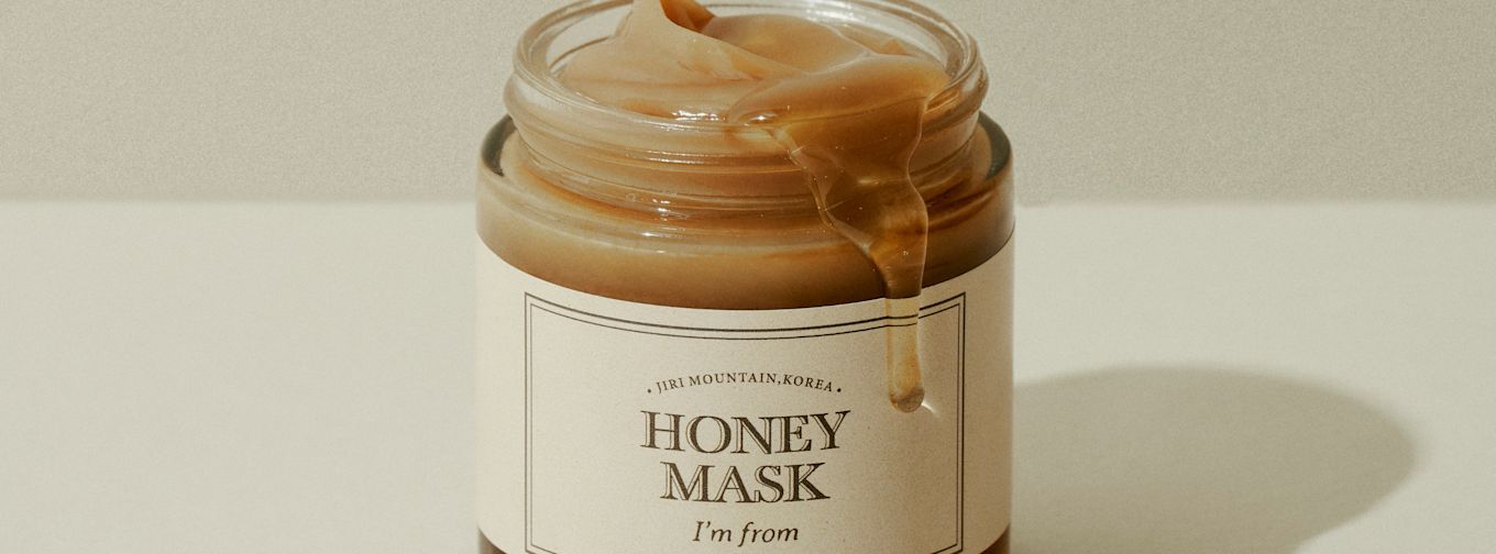Burk med ansiktsmask märkt "Honey Mask" från "I'm from", honung rinner ner längs kanten på burken mot en ljus bakgrund.