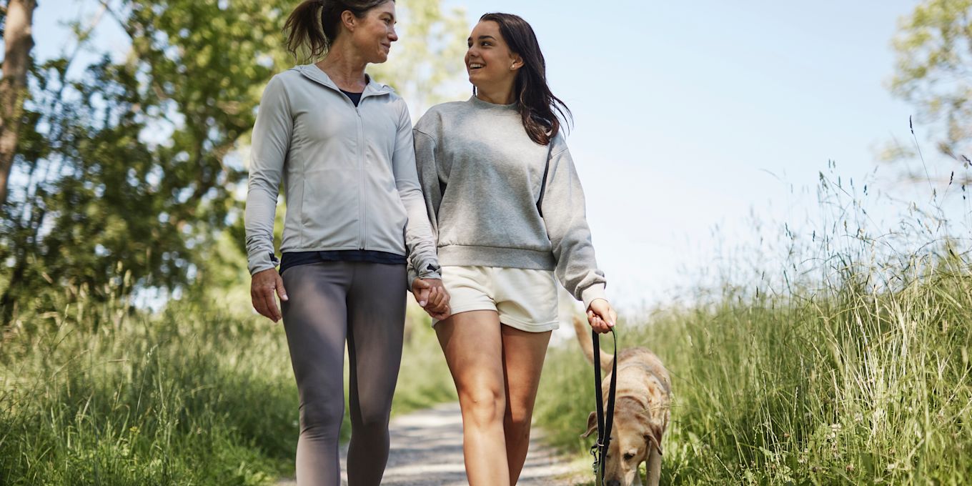 Mamma och tonårsdotter går på en promenad utomhus, tillsammans med en hund.