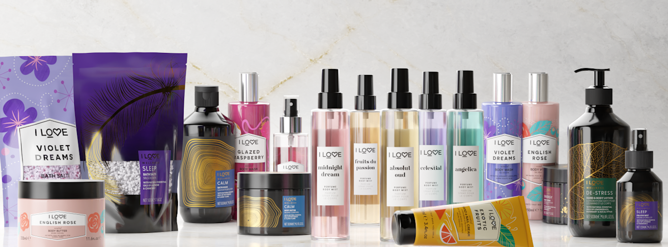 Flera I LOVE-produkter för kroppsvård, inklusive body mist, body butter, badsalt, lotion och duschgel, står uppradade på ett marmorbord.