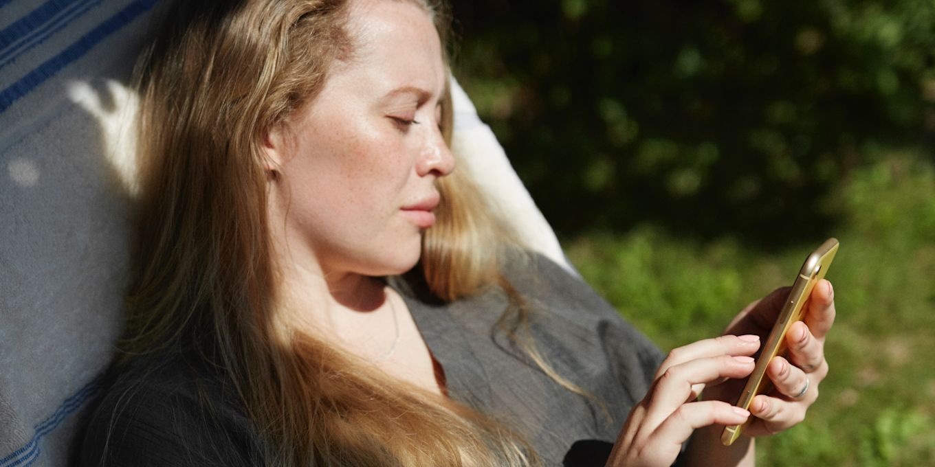 Kvinna sitter utomhus i solstol och tittar på sin mobiltelefon.