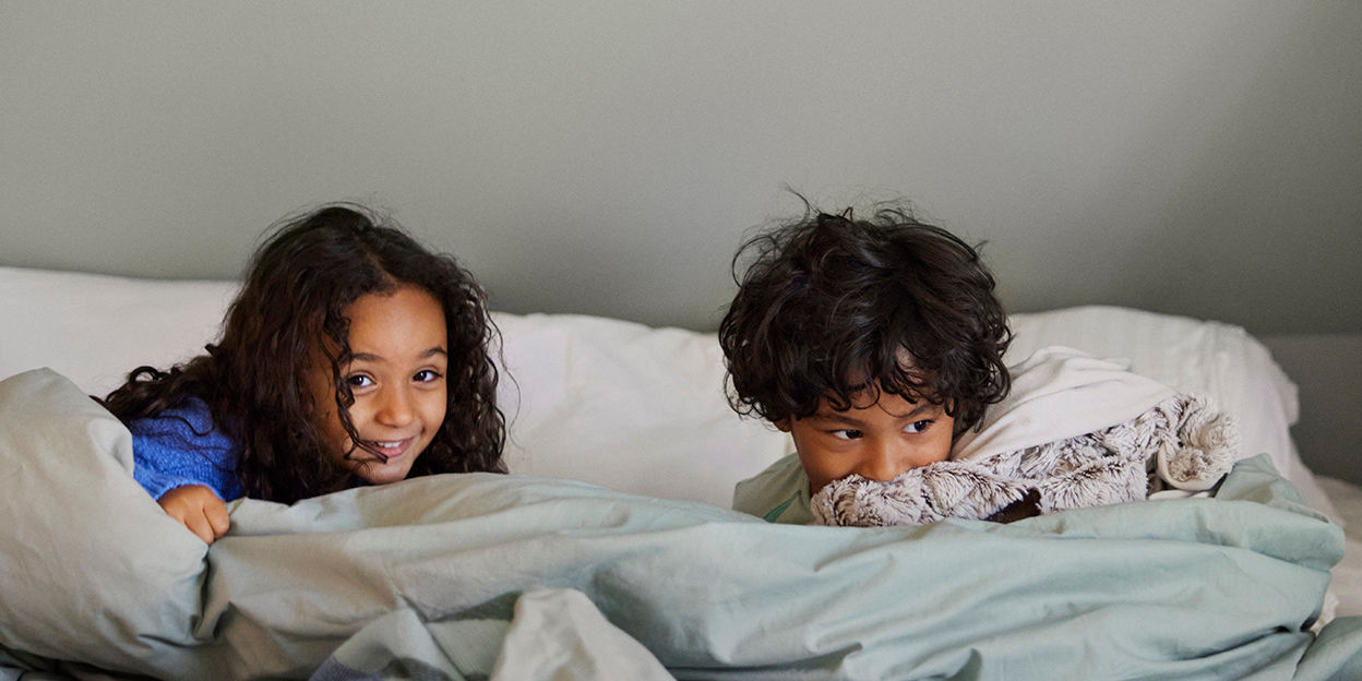 Pojke och flicka leker i sängen och tittar upp från täcket.