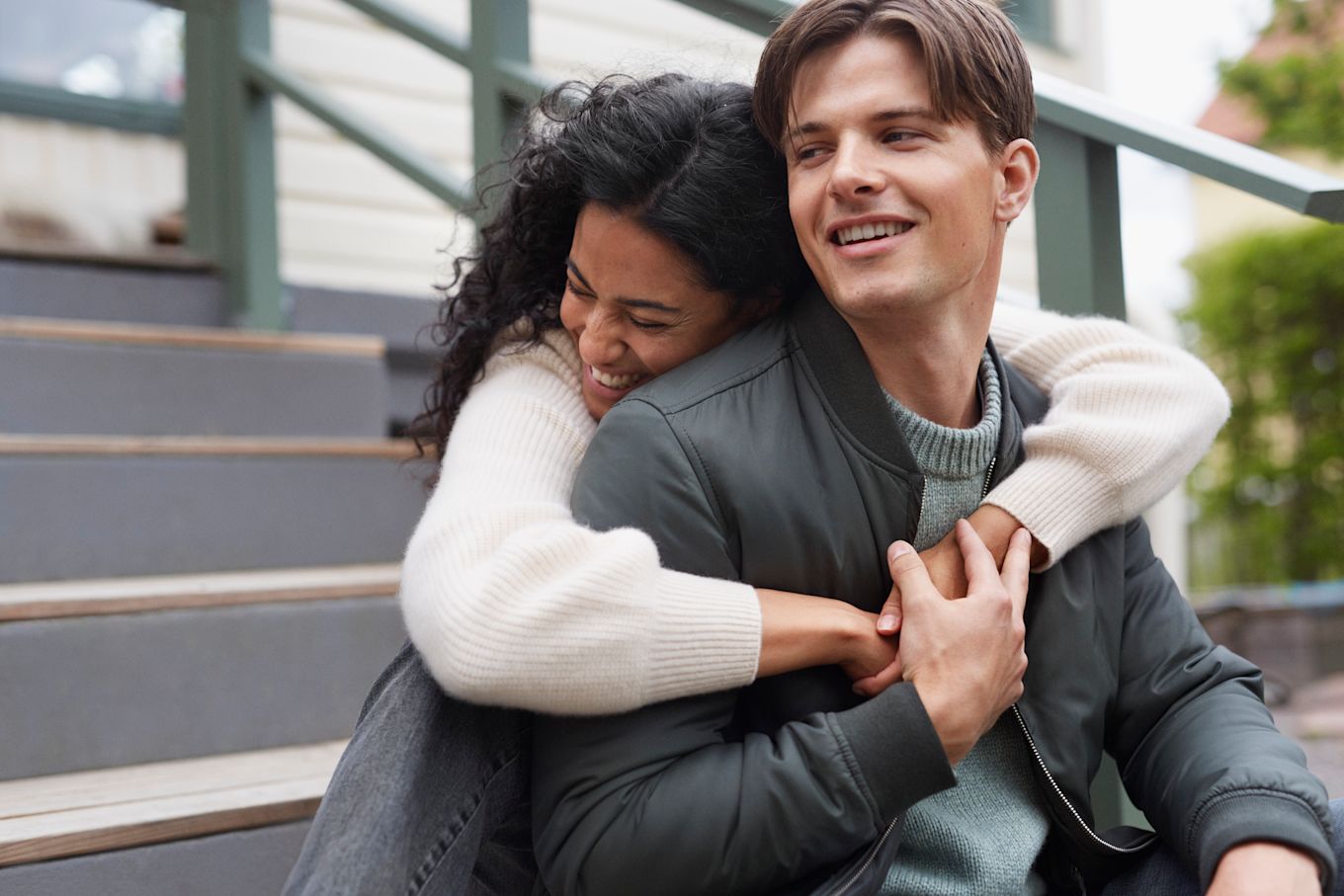 Tjej och kille sitter utomhus i en trappa och kramas och skrattar.