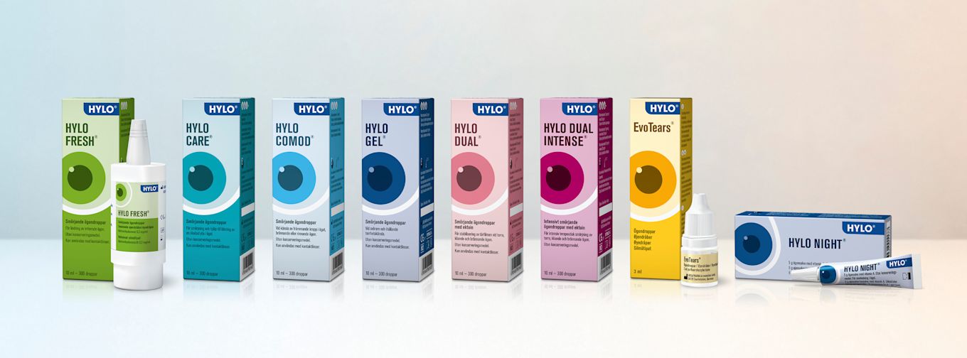 Flera förpackningar av HYLO och EvoTears ögondroppar och ögonsalva står uppradade på ett vitt underlag.