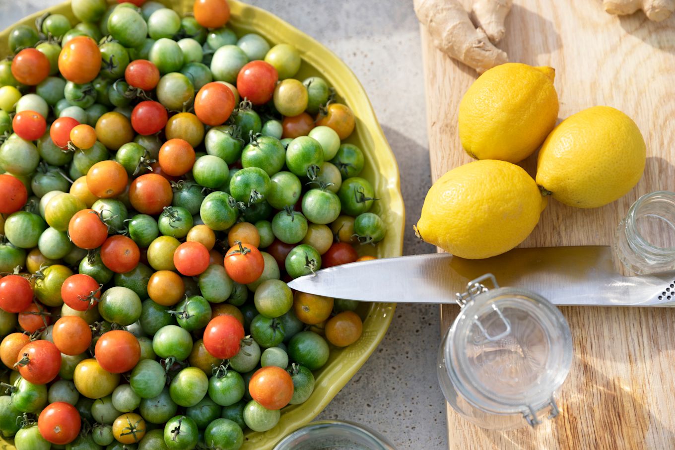Ett stort gult fat med massa små tomater i olika färger, samt en skärbräda med citroner, ingefära och en kniv.