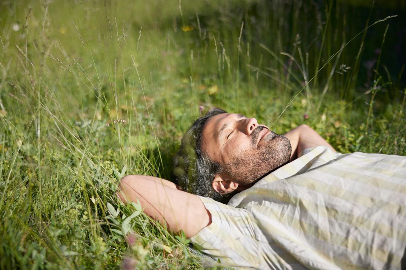 Man ligger ute på en gräsmatta på sommaren och blundar i solskenet.