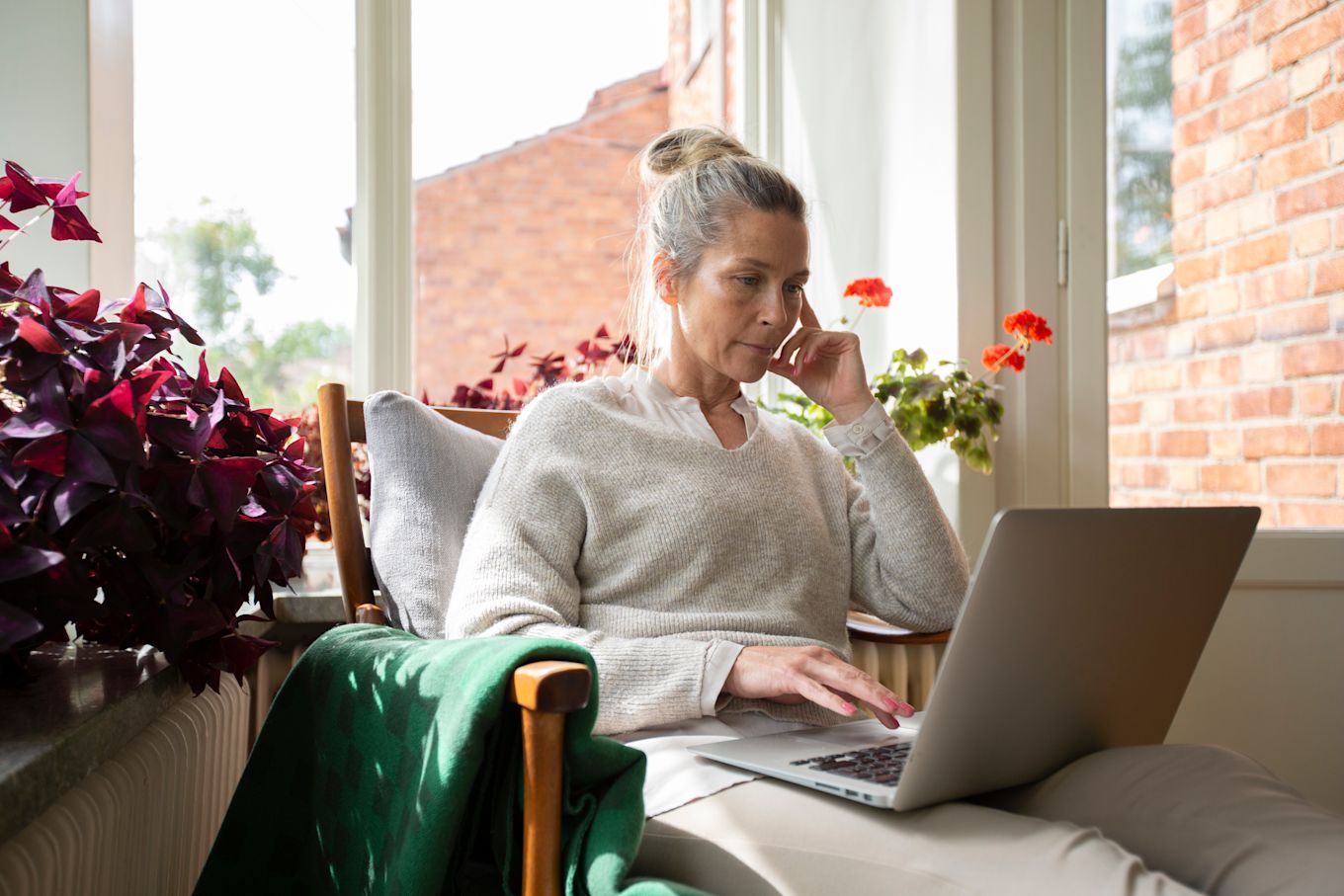 Kvinna sitter i fåtölj och tittar på en bärbar dator.