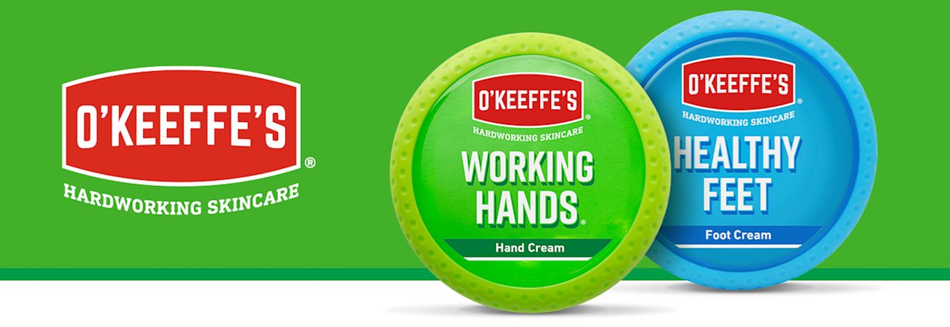 Två burkar O’Keeffe’s hudvård: Working Hands handkräm i grönt och Healthy Feet fotkräm i blått, mot grön bakgrund.