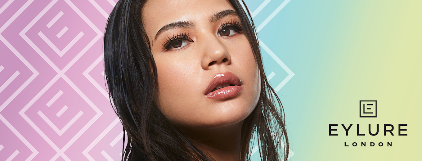 Kvinna med långa, fylliga ögonfransar och glansiga läppar poserar mot pastellfärgad bakgrund, logotypen Eylure London syns till höger.