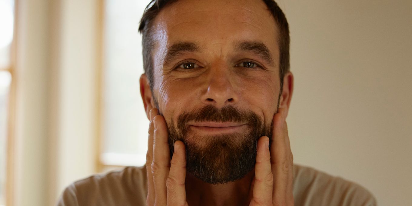 Man speglar sig i badrummet och rör vid sitt ansikte med sina händer.