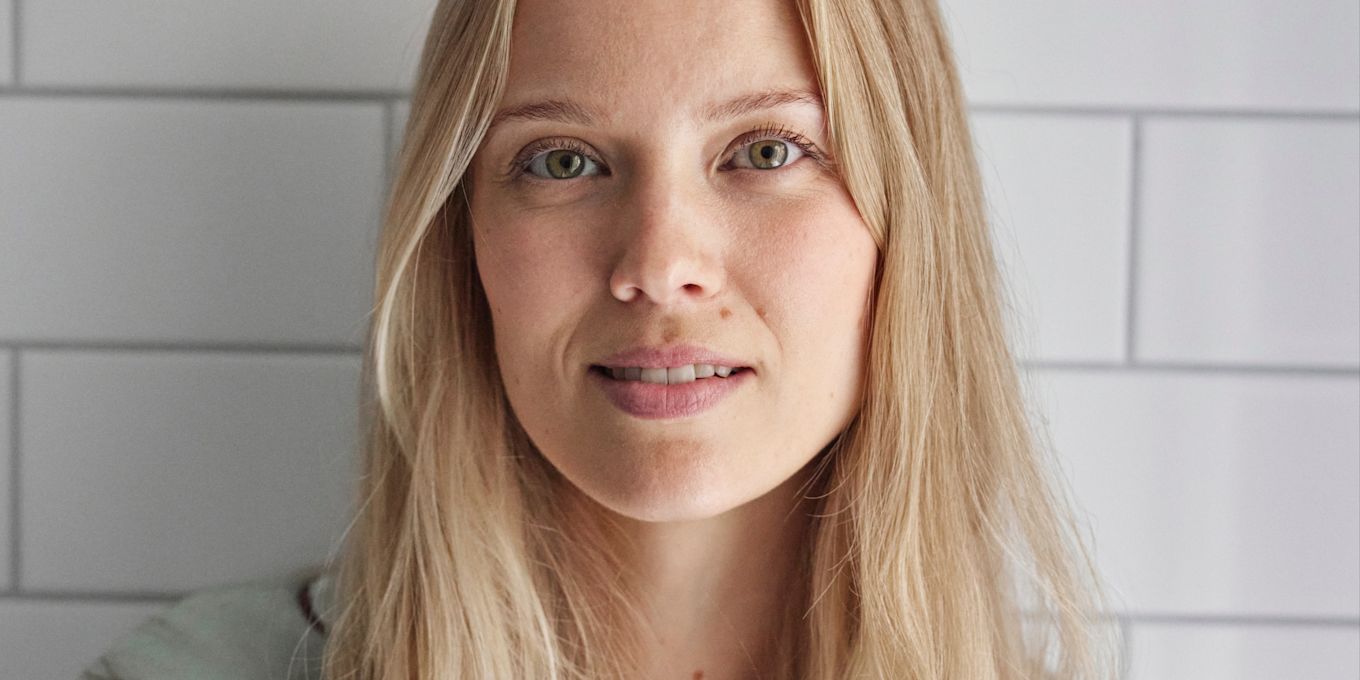 Kvinna står i ett badrum iklädd grön pyjamasskjorta.