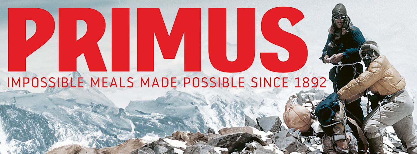 Tre bergsklättrare i vinterkläder lagar mat på en stenig bergstopp, med texten "PRIMUS IMPOSSIBLE MEALS MADE POSSIBLE SINCE 1892" ovanför.