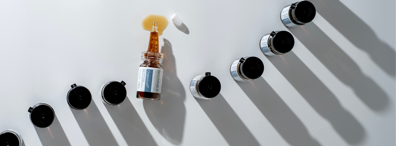 Flaska med Bionnex OrganicaO serum ligger på vit yta, omgiven av svarta lock och utspilld vätska.