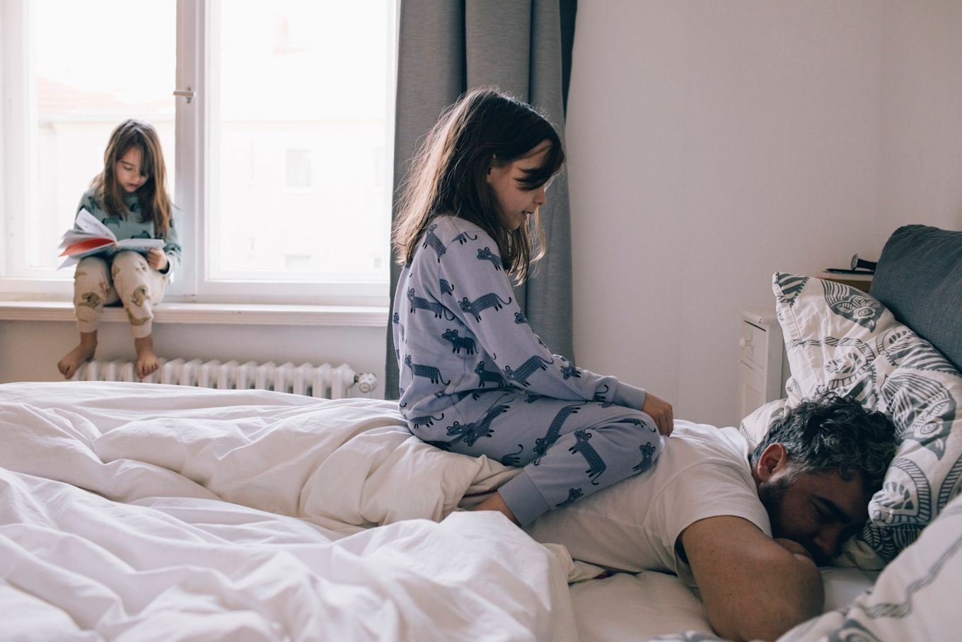 En man ligger i sängen och sover, på hans rygg sitter ett barn och leker.