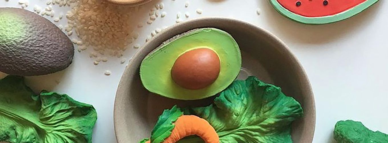 Leksaksmat i form av avokado, salladsblad, morot och vattenmelon ligger på ett vitt bord med ris runtomkring.