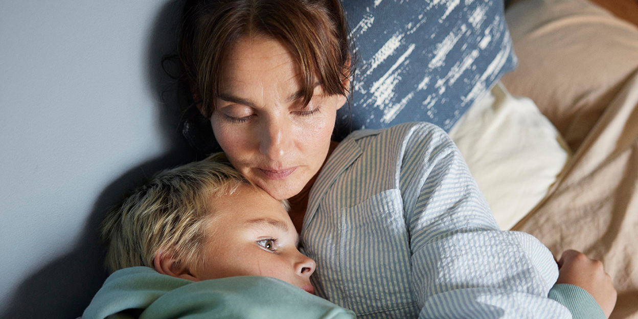 Kvinna håller om pojke i sängen. 