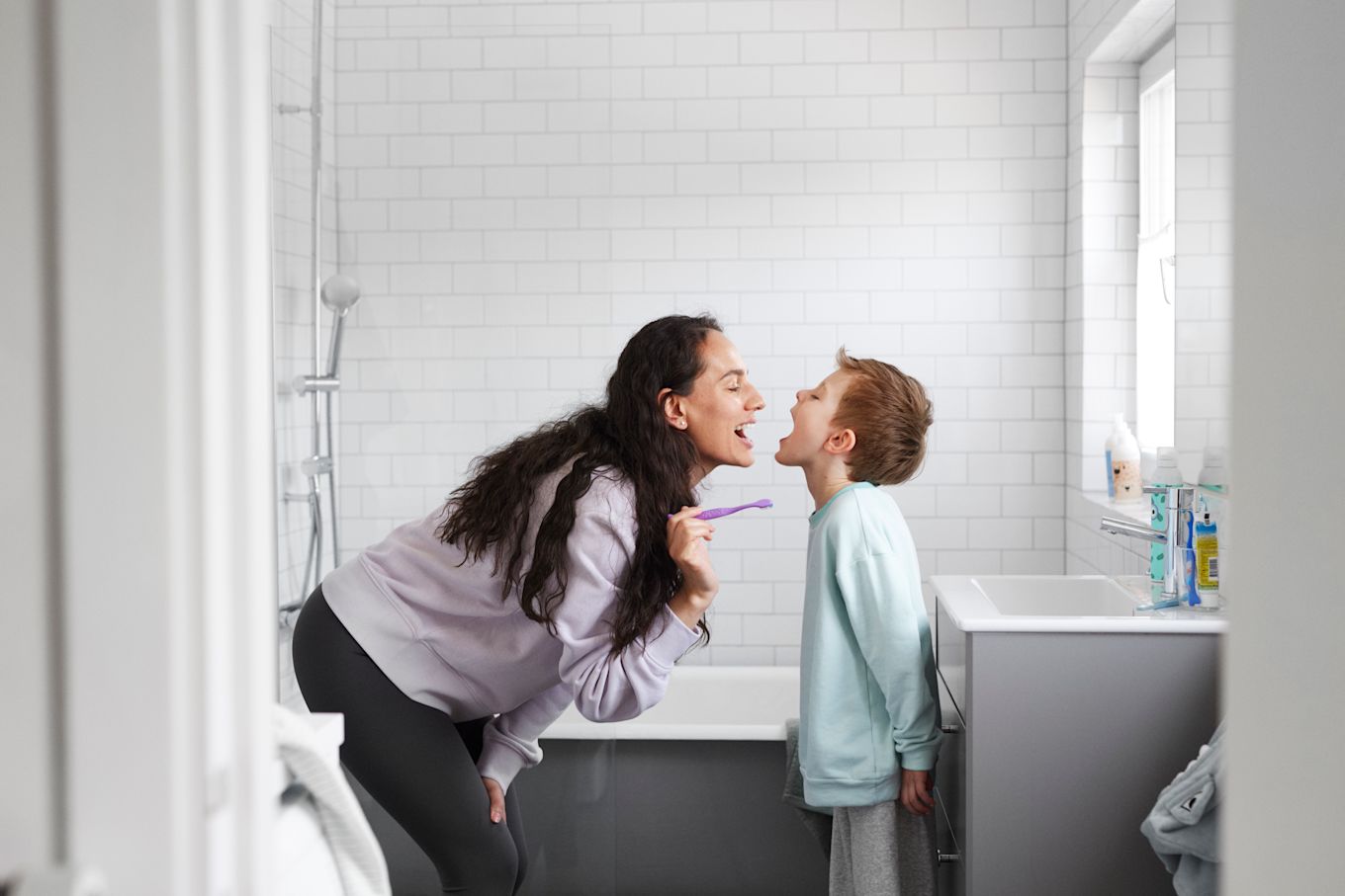 Mamma och son andas på varandra och visar sina fräscha andedräkter efter att ha borstat tänderna tillsammans.