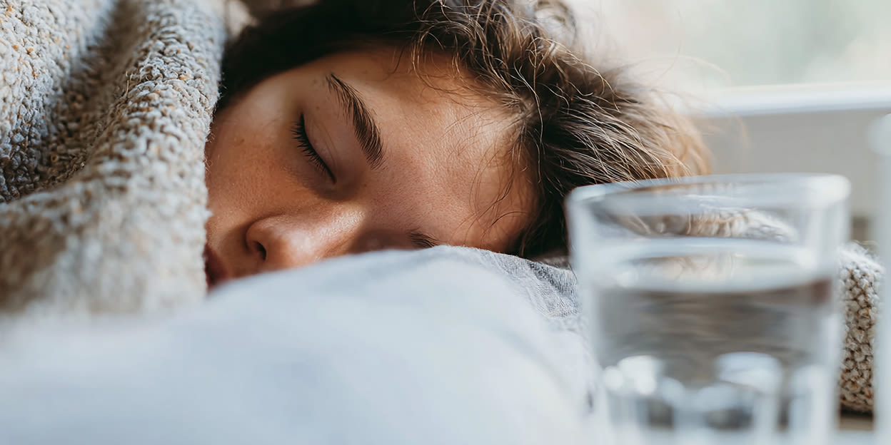 Kvinna sover under en filt med ett vattenglas bredvid sig.