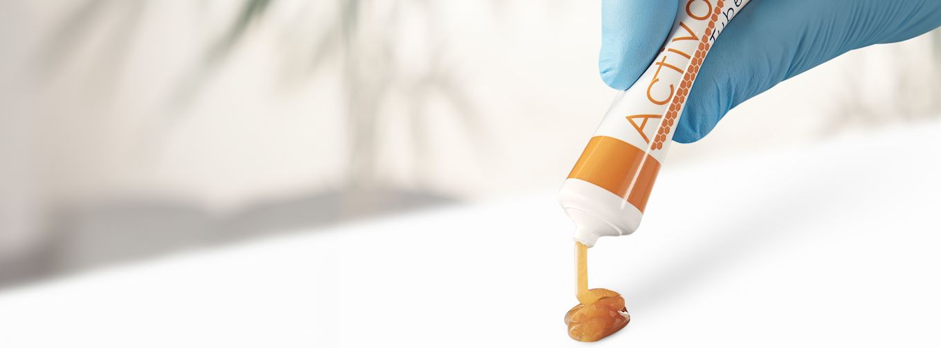 Hand med blå handske trycker ut gulaktig gel från en tub märkt "ACTIVON" på en vit yta.