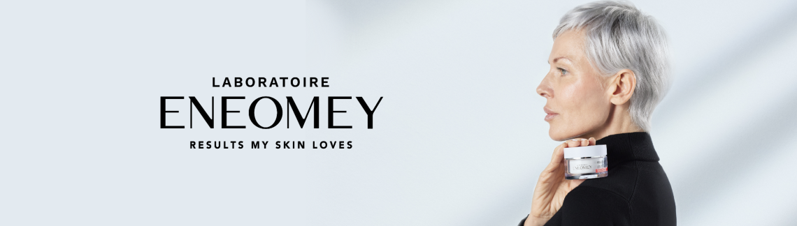 Kvinna med kort grått hår håller en burk ENEOMEY-kräm mot hakan, texten "LABORATOIRE ENEOMEY RESULTS MY SKIN LOVES" syns till vänster.