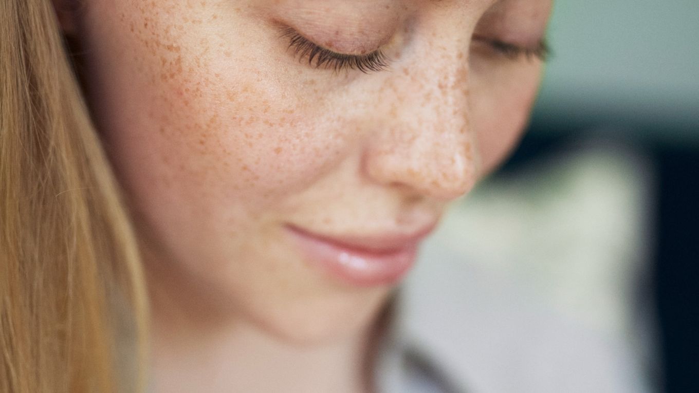 Ung tjej med fräknar som tittar ner med ett milt leende. 