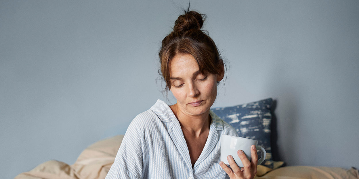 Kvinna sitter i sängen och kollar nedåt. 