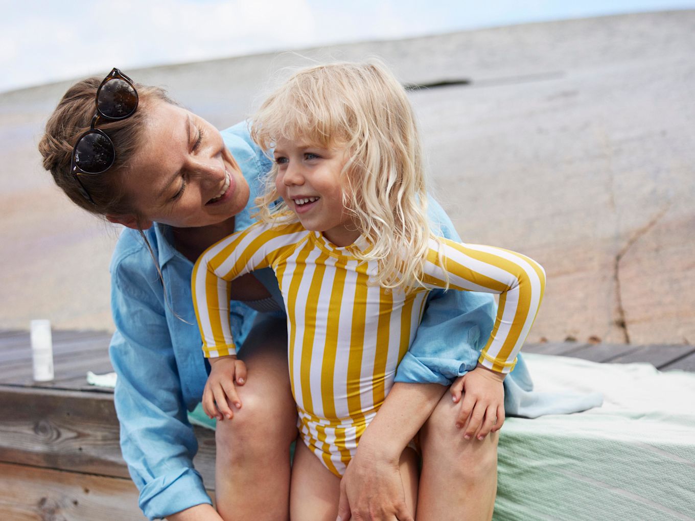 Mamma och dotter är på stranden på sommaren, mamma sitter på en bänk och kramar om dottern.