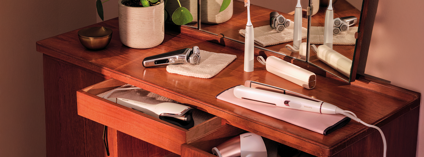 Elektriska skönhetsprodukter från Philips, inklusive rakapparat, eltandborste och hårstyler, placerade på ett trätoalettbord med spegel.