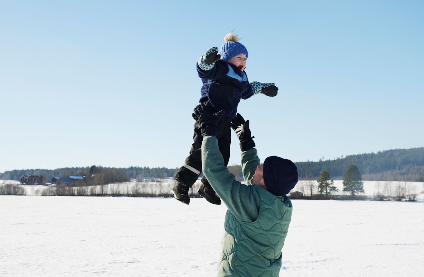 Pappa och son leker utomhus i snön, pappa kastar upp son i luften.